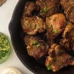 A cast iron skillet with pan seared loin lamb chops garnished with chopped parsley.