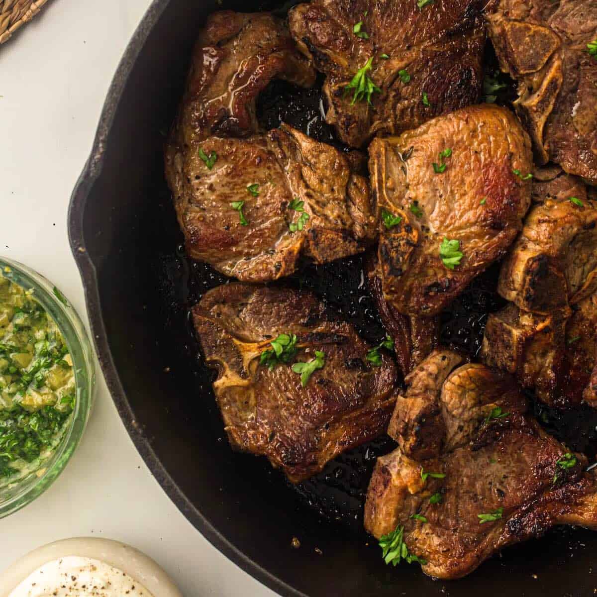 A cast iron skillet with pan seared loin lamb chops garnished with chopped parsley.