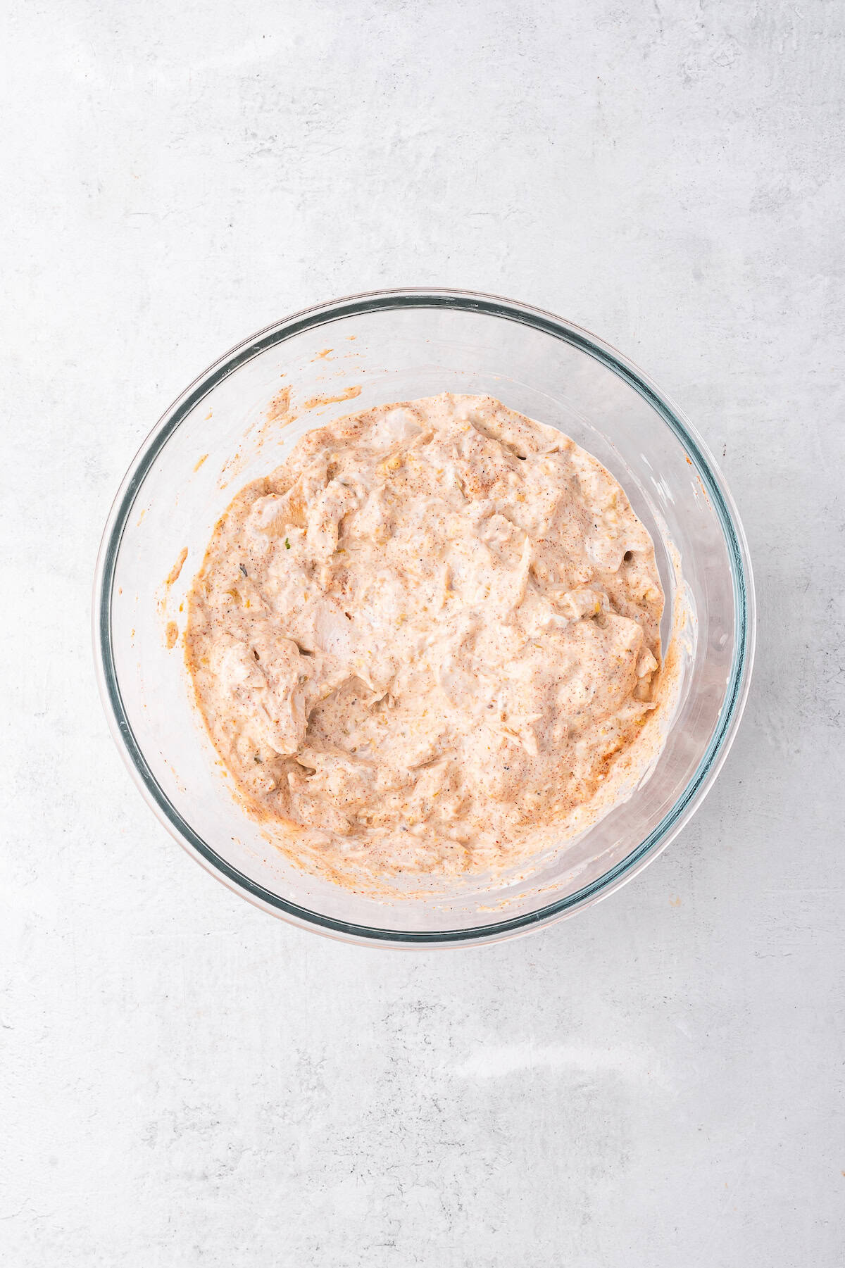 A clear glass bowl full of chicken, salsa verde, sour cream, and seasonings. 