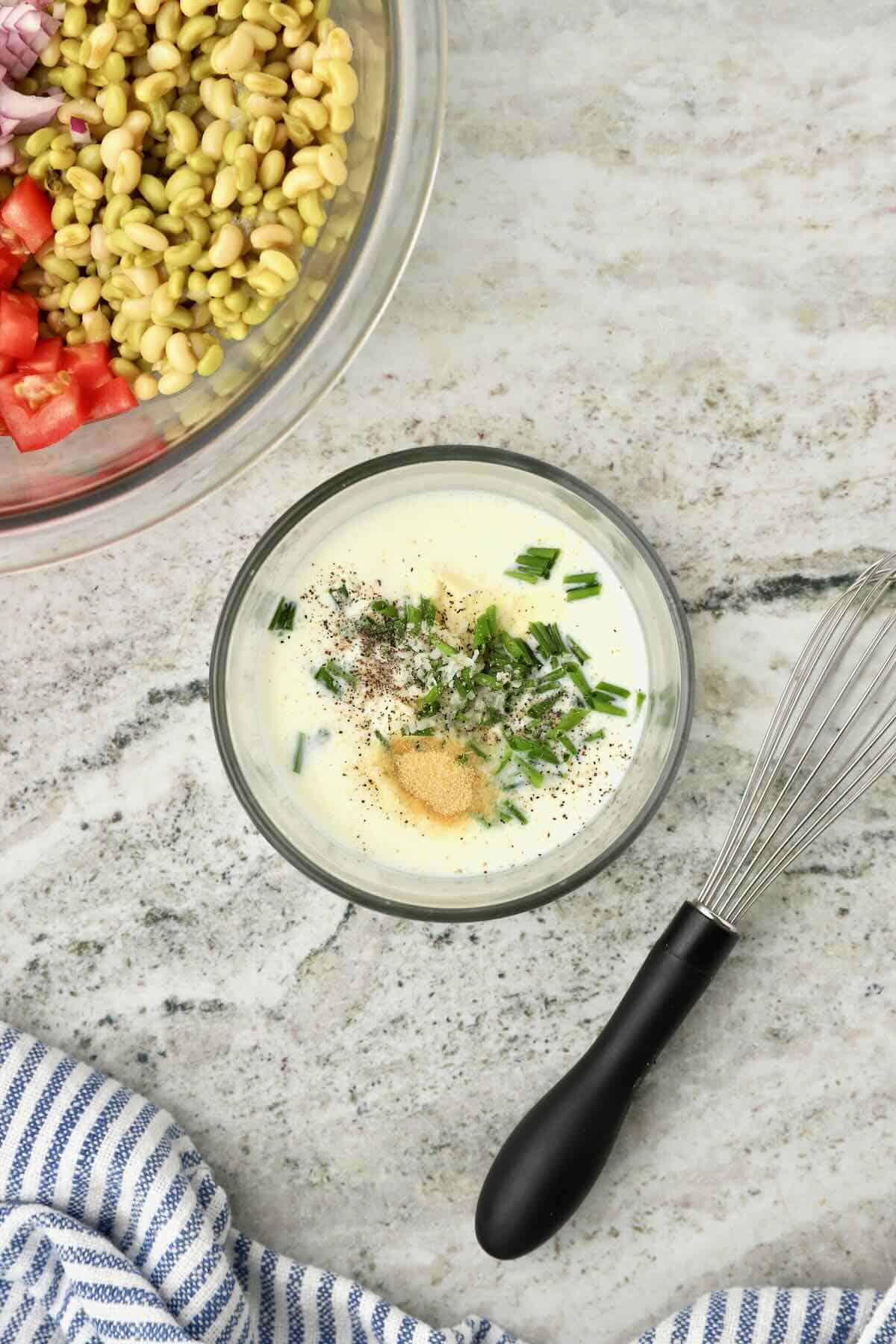 Ingredients for herb buttermilk dressing are in a small glass bowl, ready to be whisked together. 