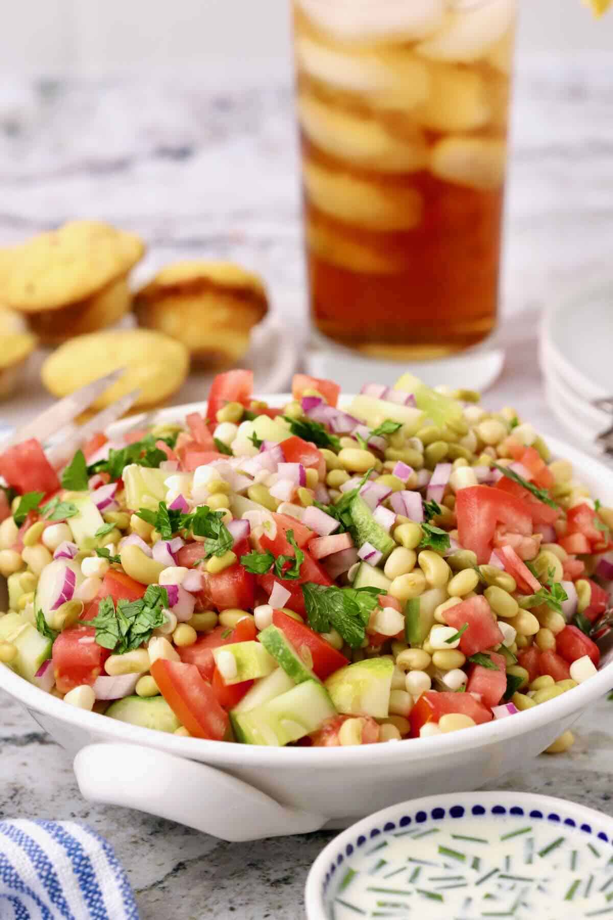 A large white bowl full of Southern Pea Salad made with white acre peas, with a glass of tea in the rear.