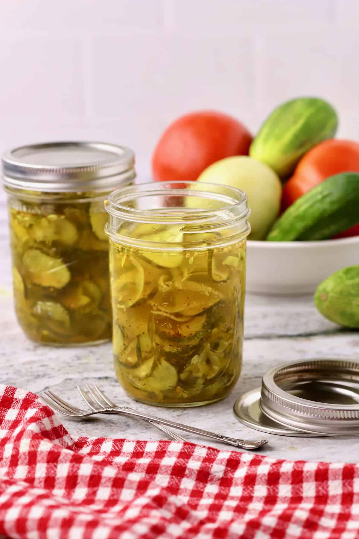 Two pint jars of microwaved bread and butter pickles on a counter with cucumbers.