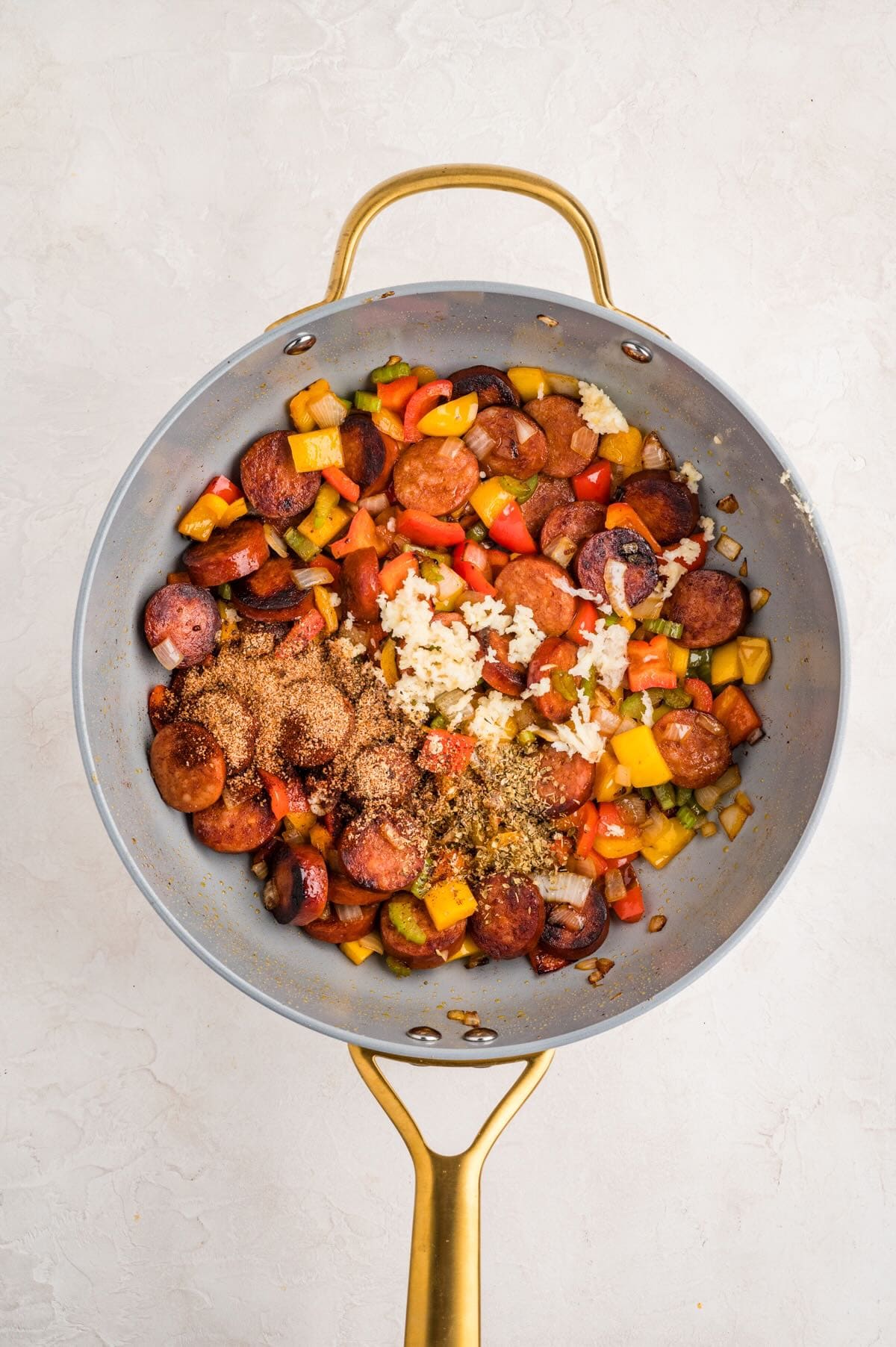 Garlic and seasonings added to browned sliced sausage and veggies in a skillet. 

