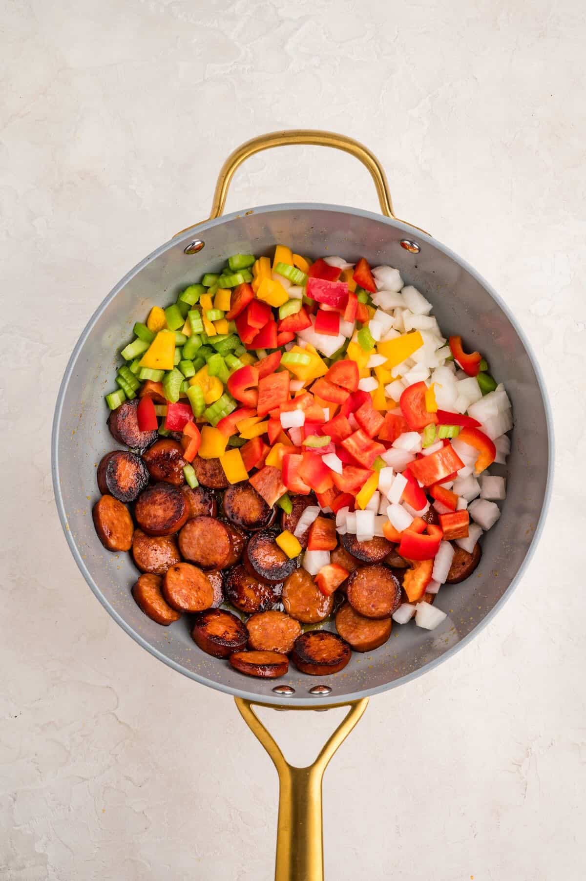 Cooking veggies with browned smoked sausage in a skillet. 