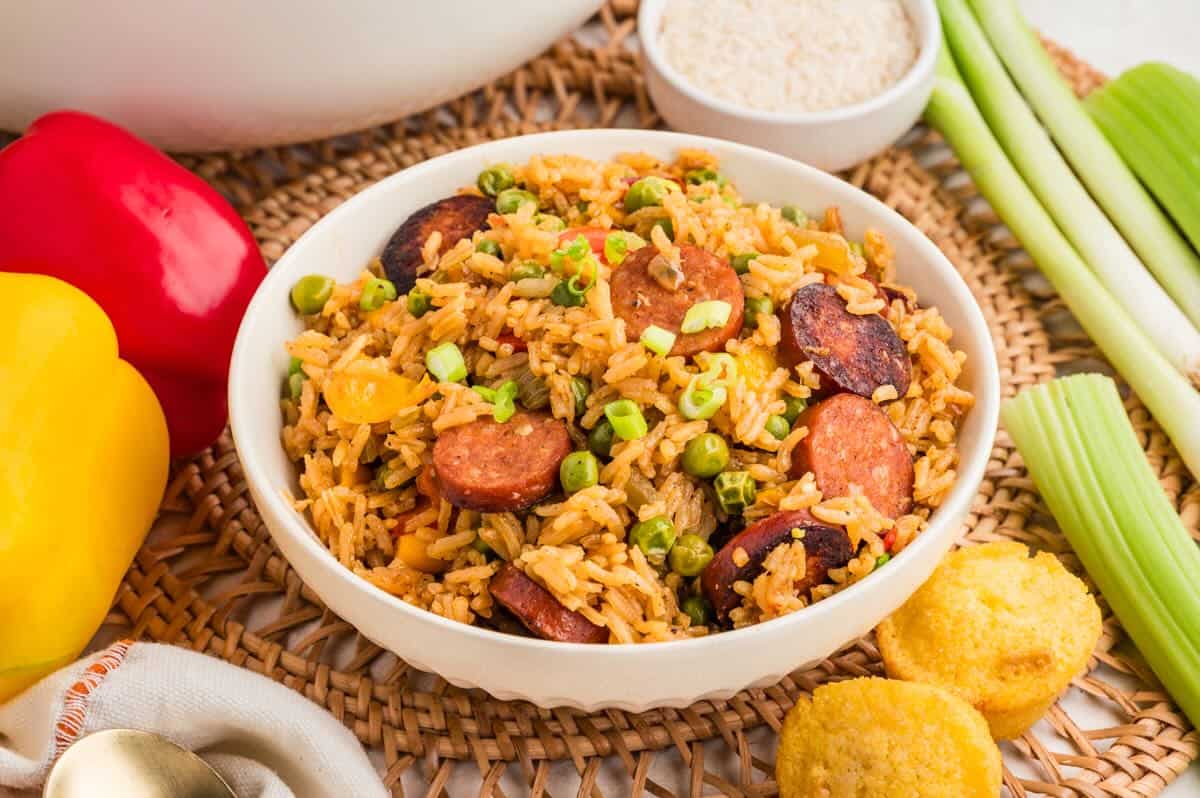 Cajun sausage and rice in a white bowl with veggies, garnished with sliced green onions.