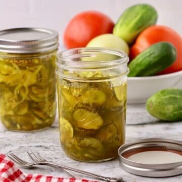 Two jars of microwave bread and butter pickles, accompanied by a bowl of cucumbers and tomatoes.