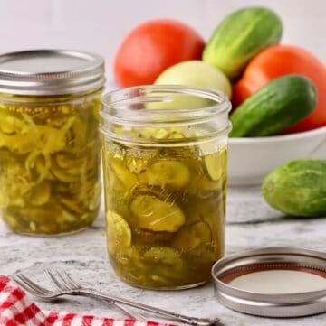 Two jars of microwave bread and butter pickles, accompanied by a bowl of cucumbers and tomatoes.