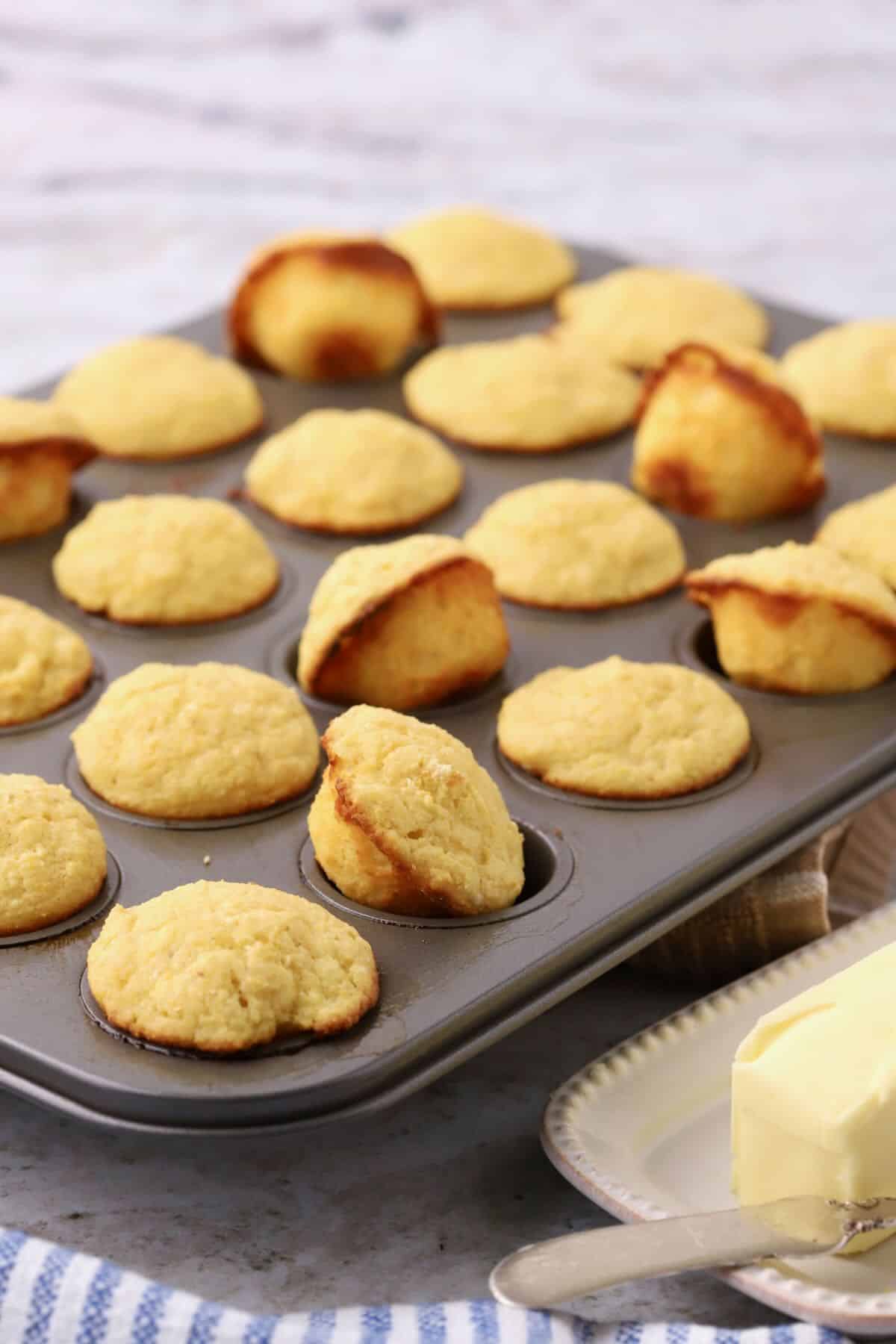 A mini muffin tin with baked mini cornbread muffins, with some on their side. 