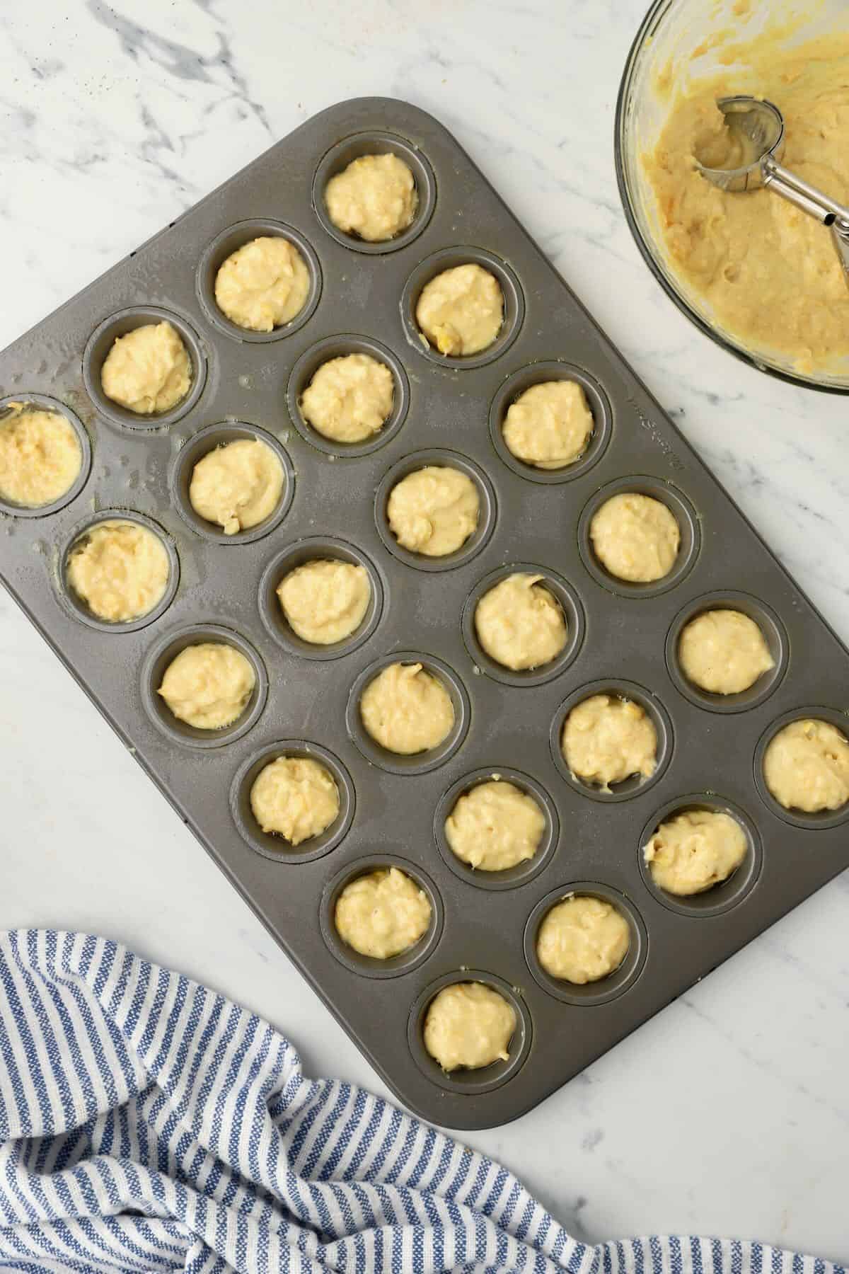 A mini muffin pan with 24 cups full of cornbread muffin batter. 