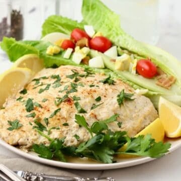 Oven baked grouper fillets topped with Parmesan and sour cream on a plate with a wedge salad.