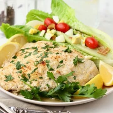 Oven baked grouper fillets topped with Parmesan and sour cream on a plate with a wedge salad.