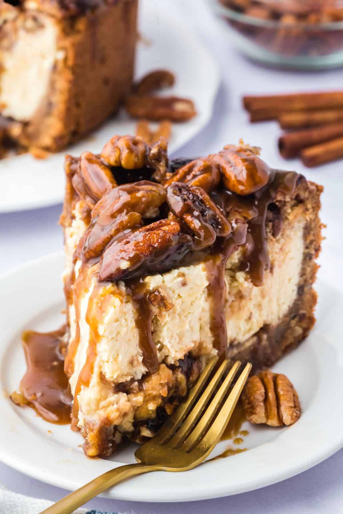 A slice of pecan pie cheesecake with a pecan crust on a white plate with a gold fork. 