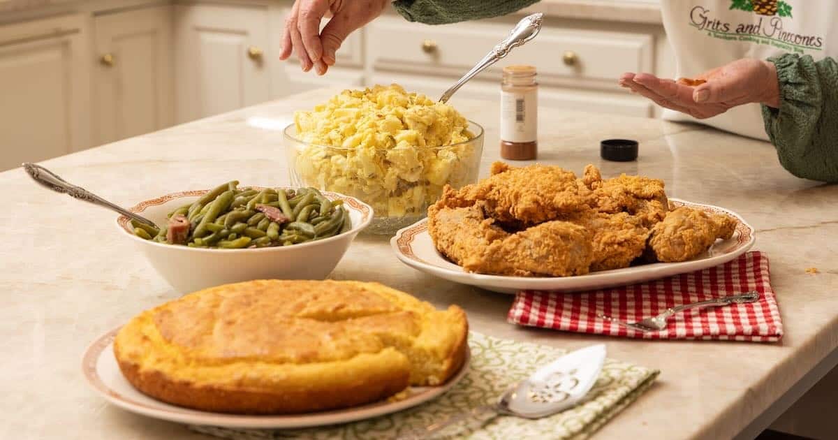 A southern dinner of fried chicken, green beans, cornbread, and potato salad on a kitchen counter. 