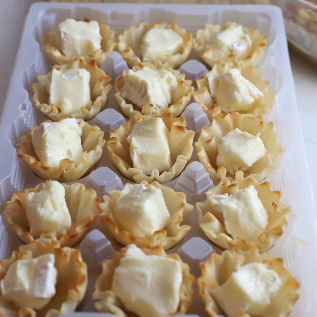 A tray of phyllo cups filled with cubes of brie cheese. 