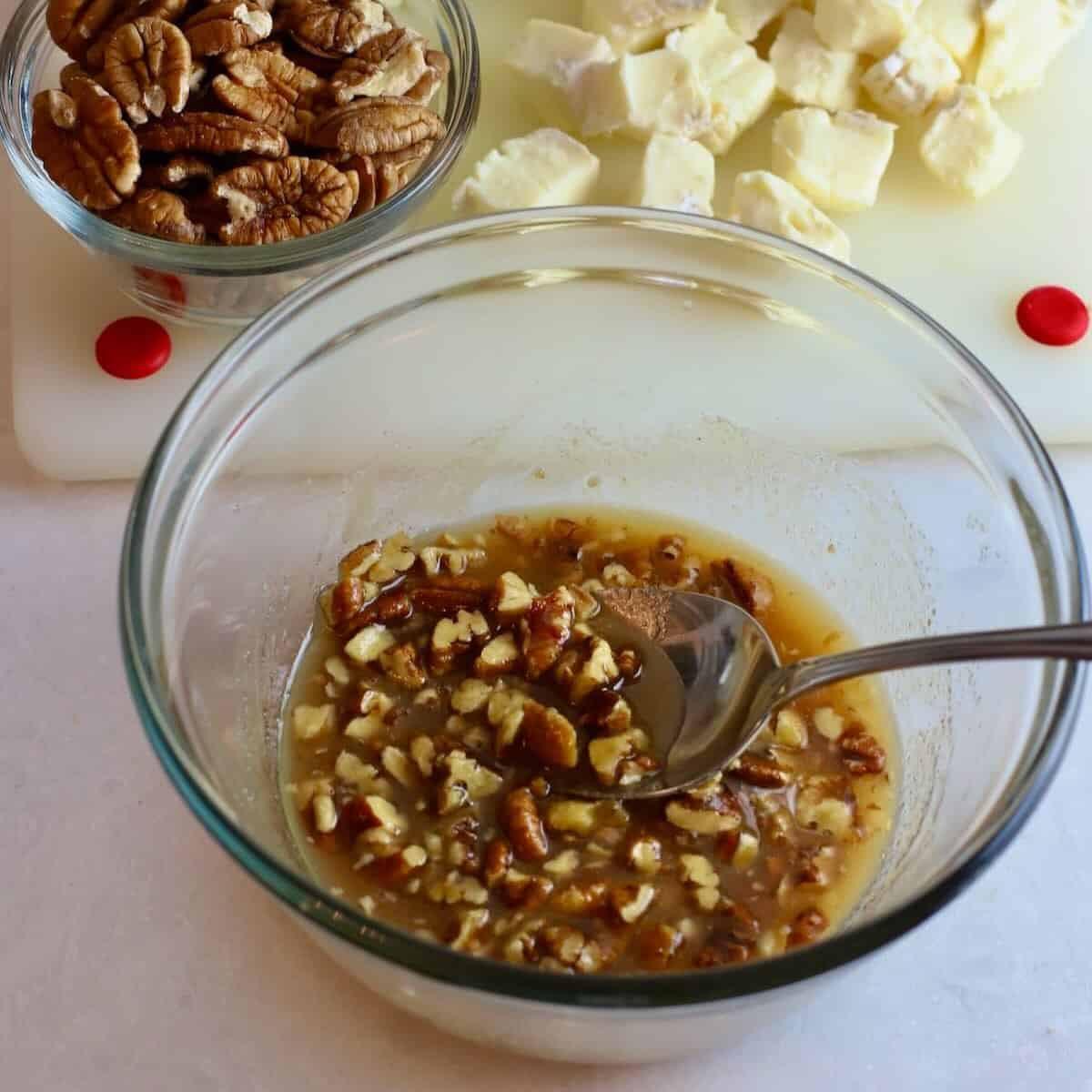 A small glass bowl with melted butter, bourbon, brown sugar, and pecans. 