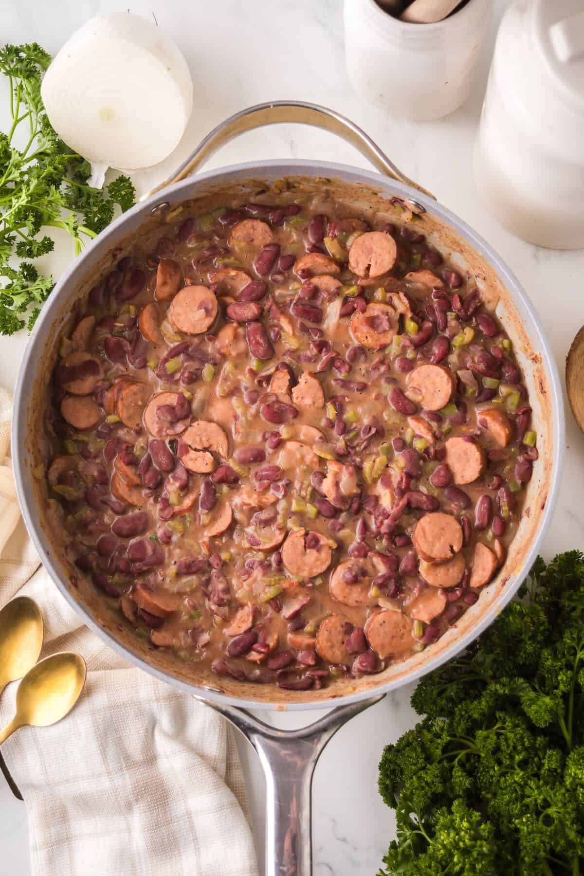 A skillet full of cooked creamy red kidney beans with vegetables is ready to be served over rice. 
