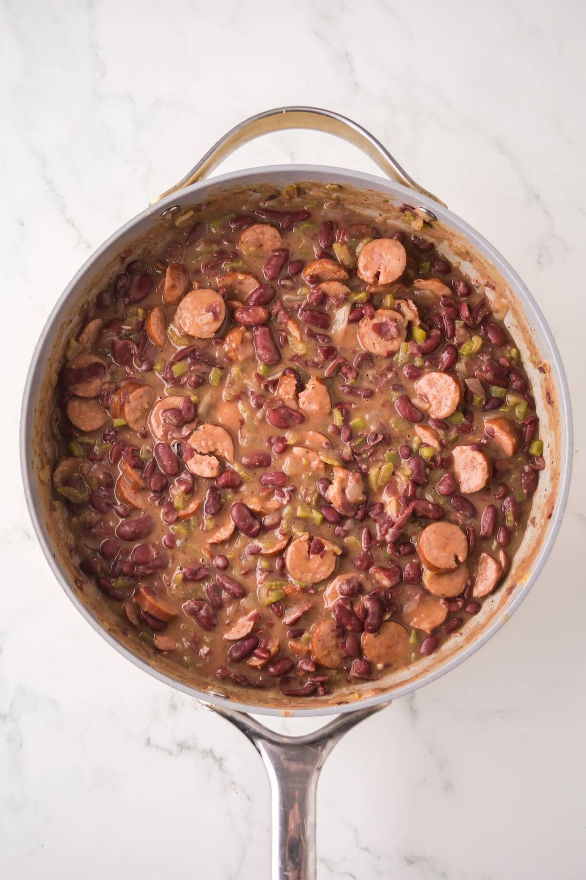 Red kidney beans are cooking along with vegetables in a skillet. 