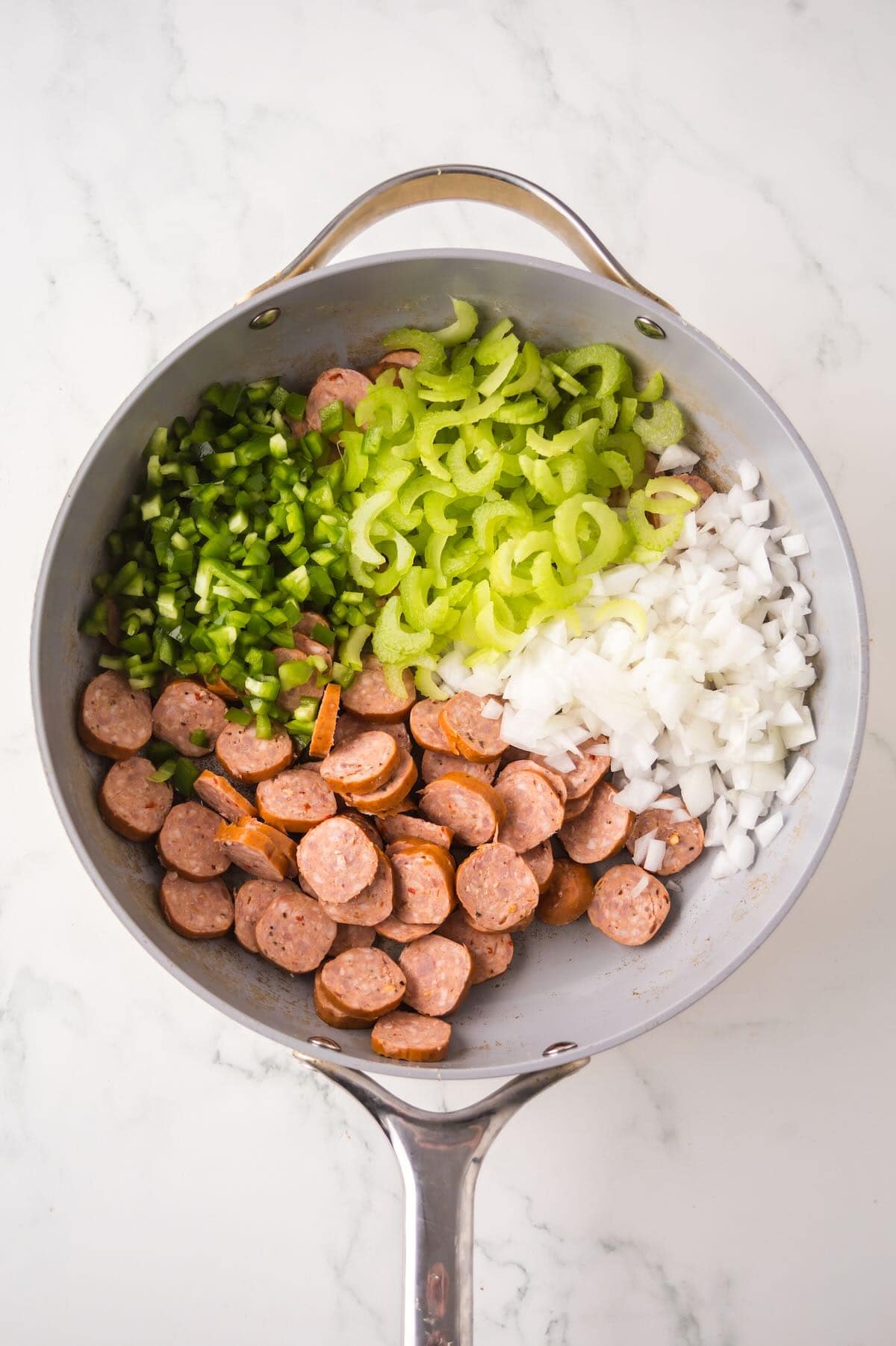 Chopped celery, green bell pepper, and onion, along with sliced sausage, in a skillet. 