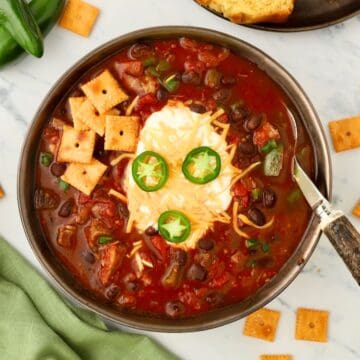 Wide bowl of chuck roast chili topped with cheese, green onions, and sour cream, served with cornbread on the side.