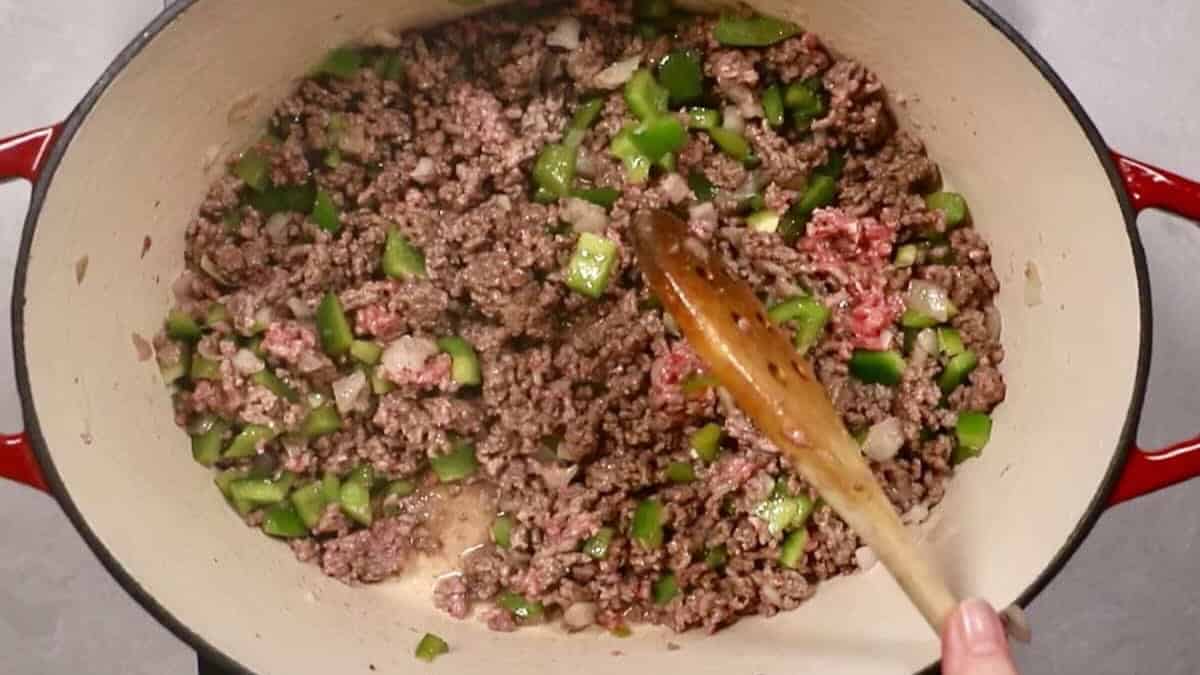 A Dutch oven with browned ground beef, bell pepper, and onion.