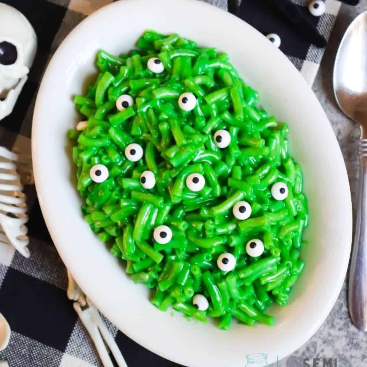 Green macaroni topped with candy eyeballs in a bowl.
