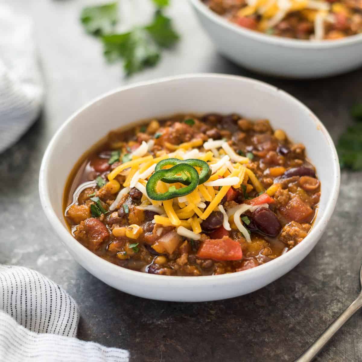 Pumpkin chili in a bowl topped with sliced jalapenos and cheese. 