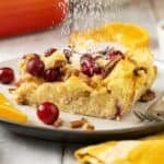 A serving of Brioche French Toast Casserole on a plate with powdered sugar being sprinkled over the top.