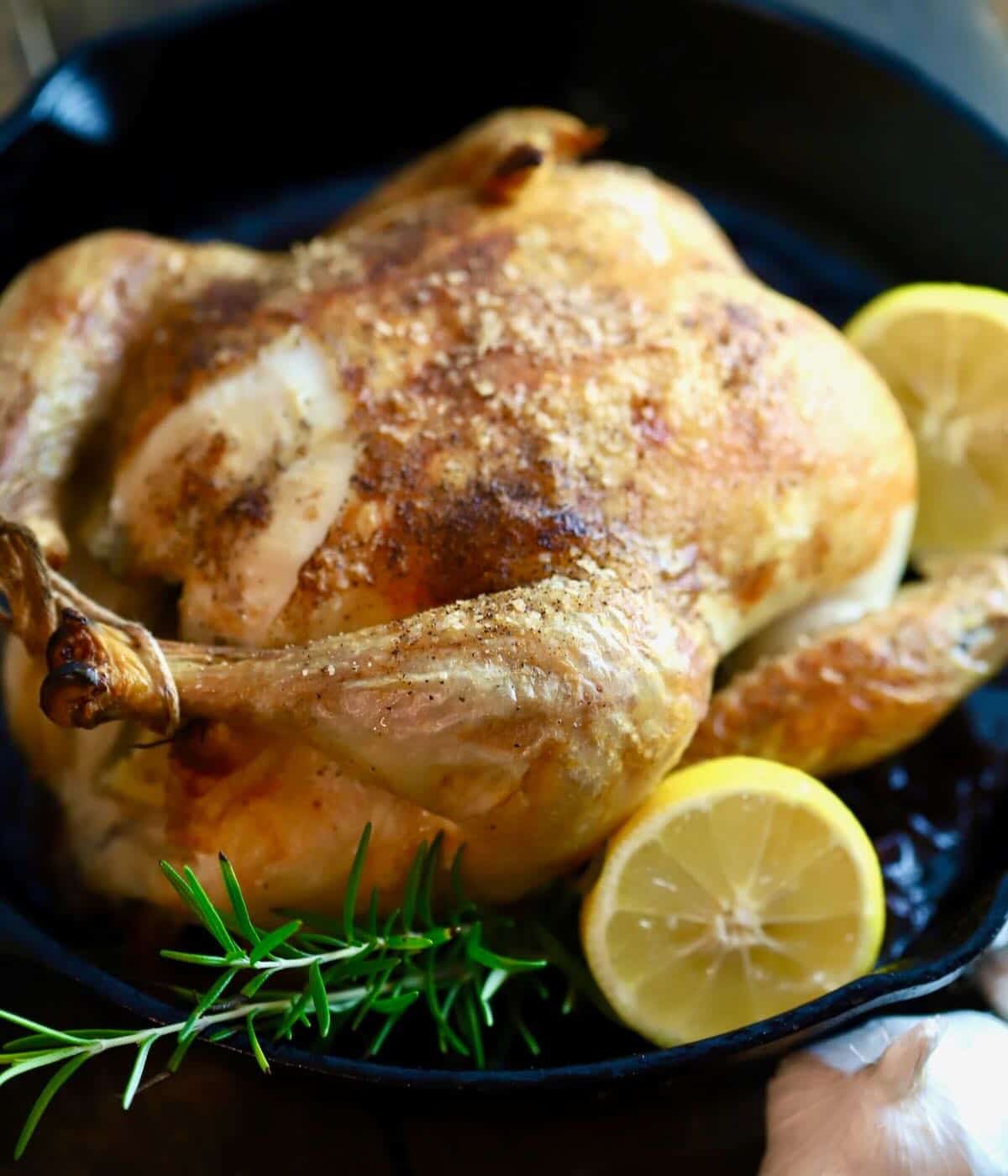 A roasted chicken with golden brown crispy skin in a cast iron skillet.