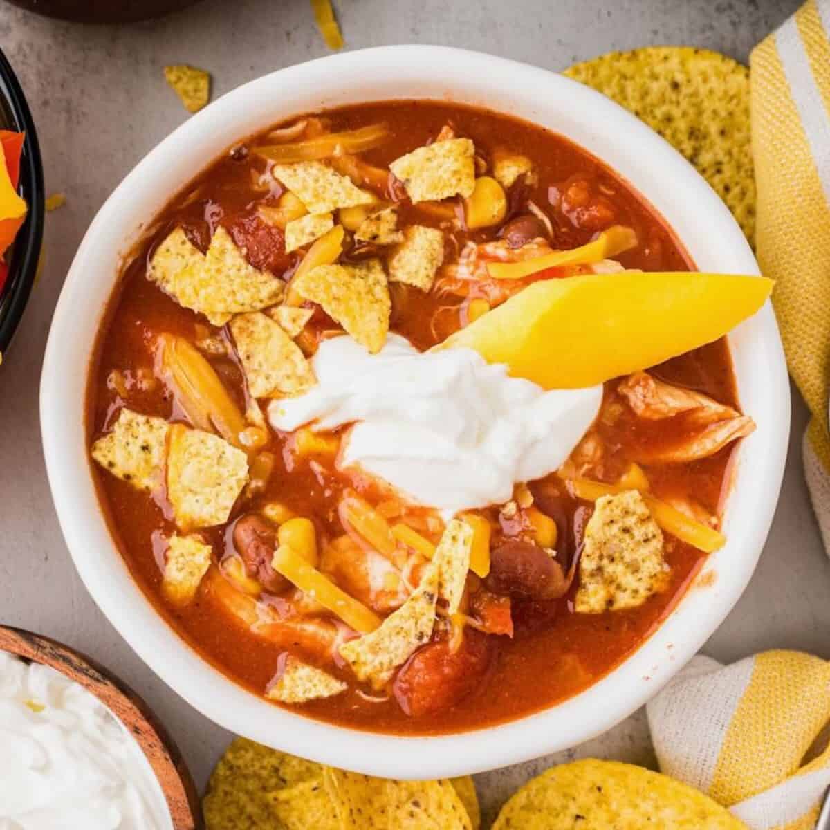 A bowl of slow cooker chicken taco soup topped with sour cream and a piece of yellow bell pepper.
