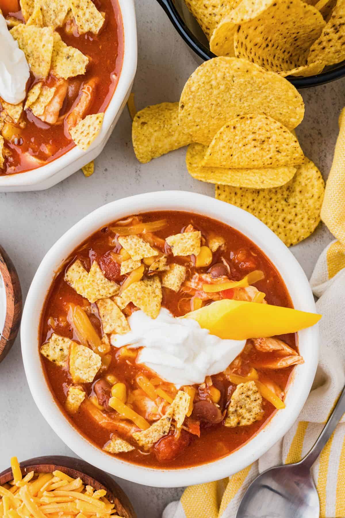 Two bowls of chicken taco soup cooked in a slow cooker, topped with sour cream and tortilla chips.