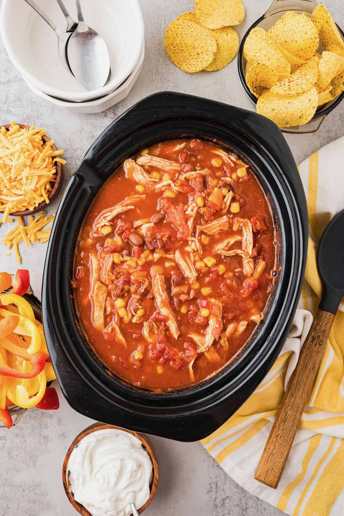 A slow cooker full of chicken taco soup, with tortilla chips scattered around.