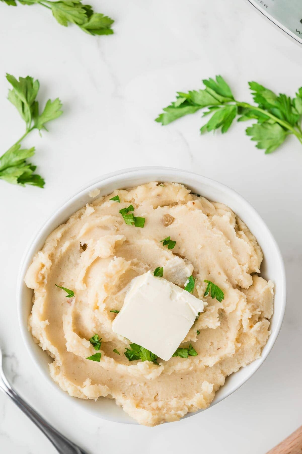A white bowl full of mashed potatoes cooked in a crock pot with a pat of butter in the middle.