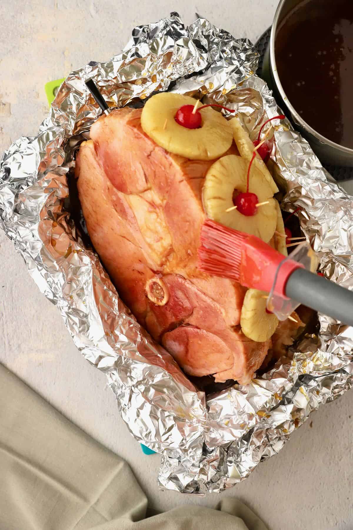 Using a long handled pastry brush to apply maple glaze to a ham. 