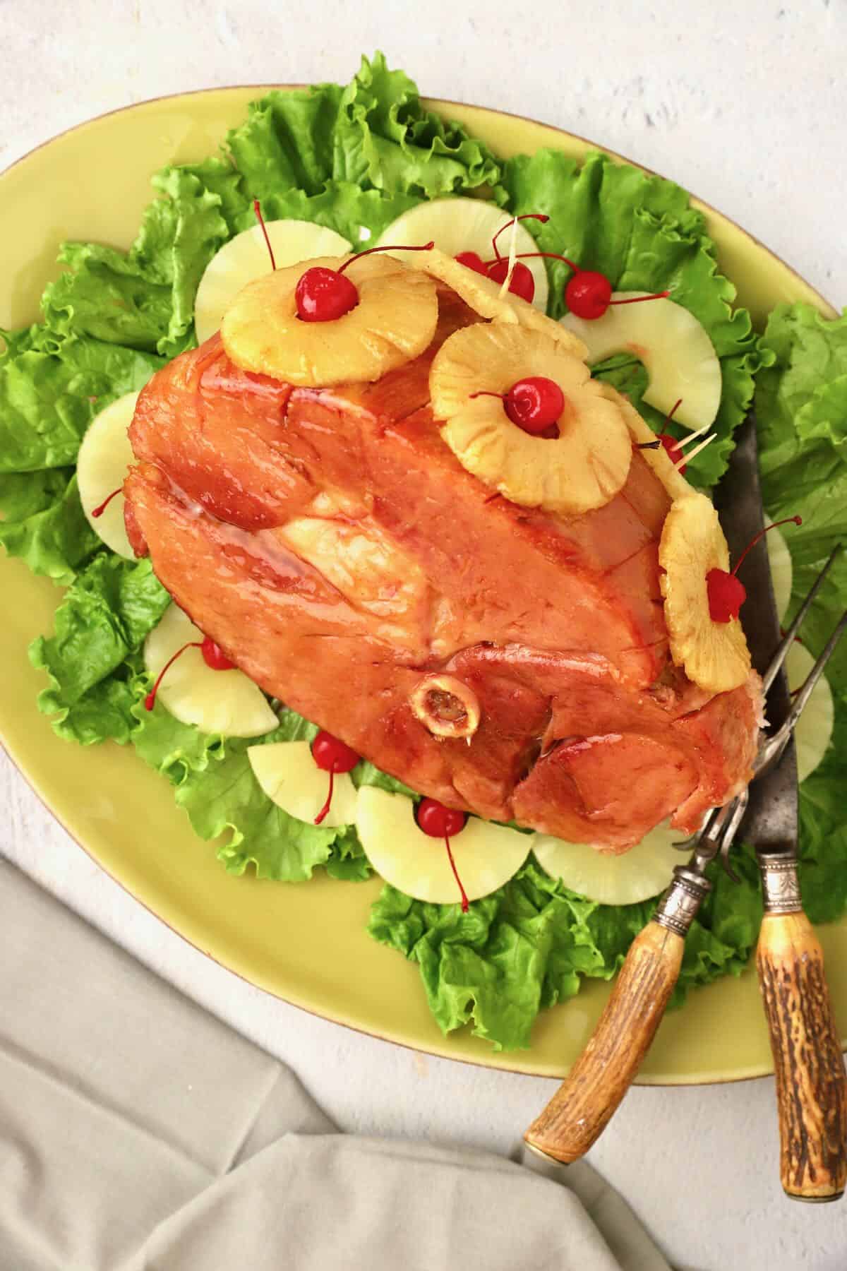 Baked Maple Glazed Ham on a platter garnished with pineapple rings and cherries. 