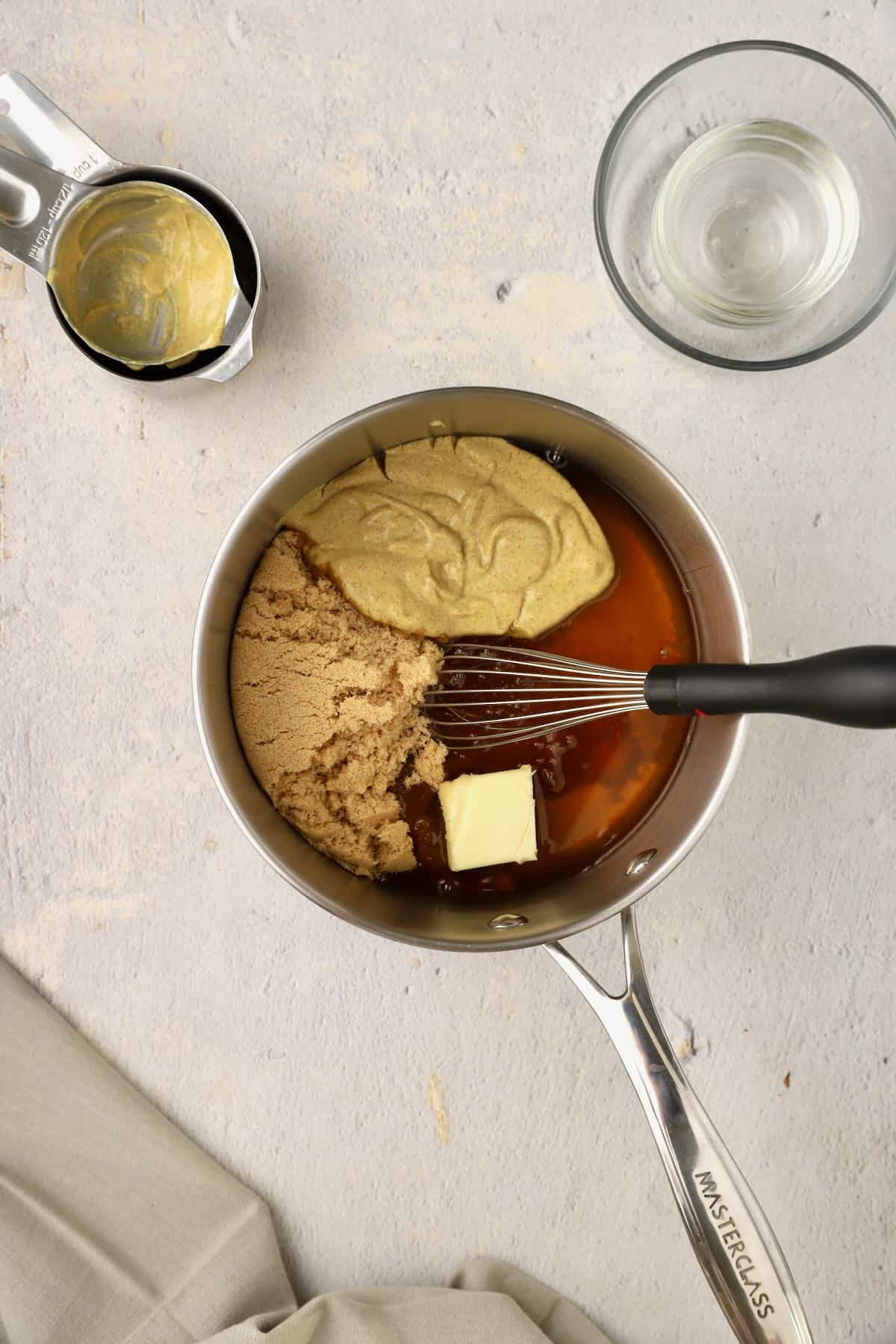 Glaze ingredients in a saucepan include maple syrup, brown sugar, Dijon mustard, and apple cider vinegar. 