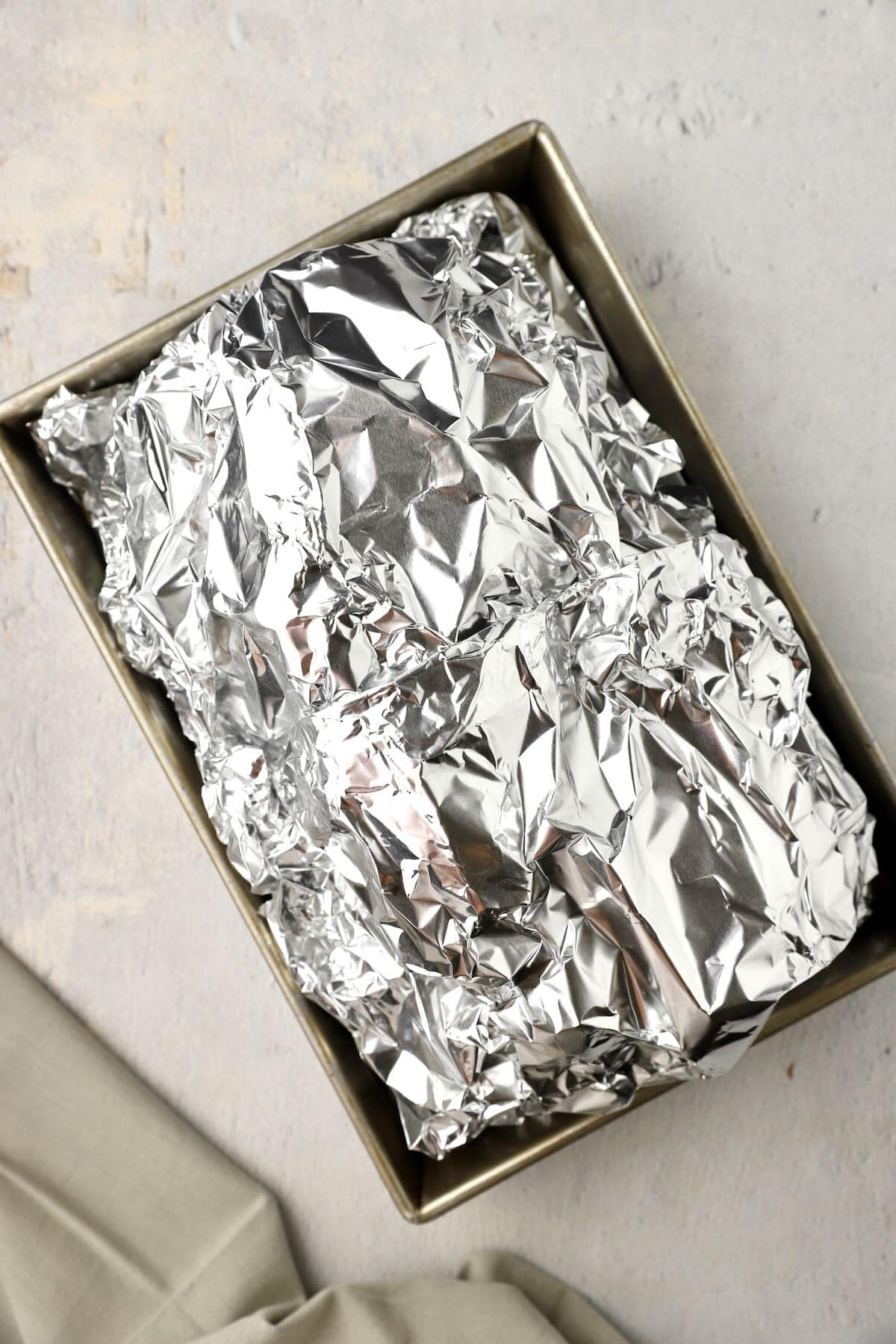 A ham is completely enclosed in foil to bake in the oven. 