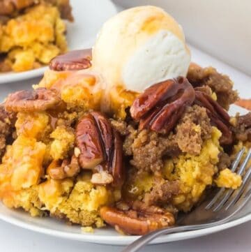 A serving of pecan pie dump cake on a plate, topped with a scoop of ice cream and caramel sauce.