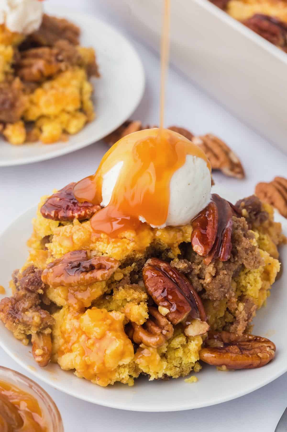 A serving of pecan pie dump cake on a plate topped with a scoop of ice cream and a caramel drizzle. 