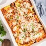 A large pan of baked ravioli topped with melted cheese and chopped parsley.