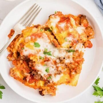 A large serving of baked ravioli topped with melted mozzarella cheese and garnished with chopped parsley on a plate.