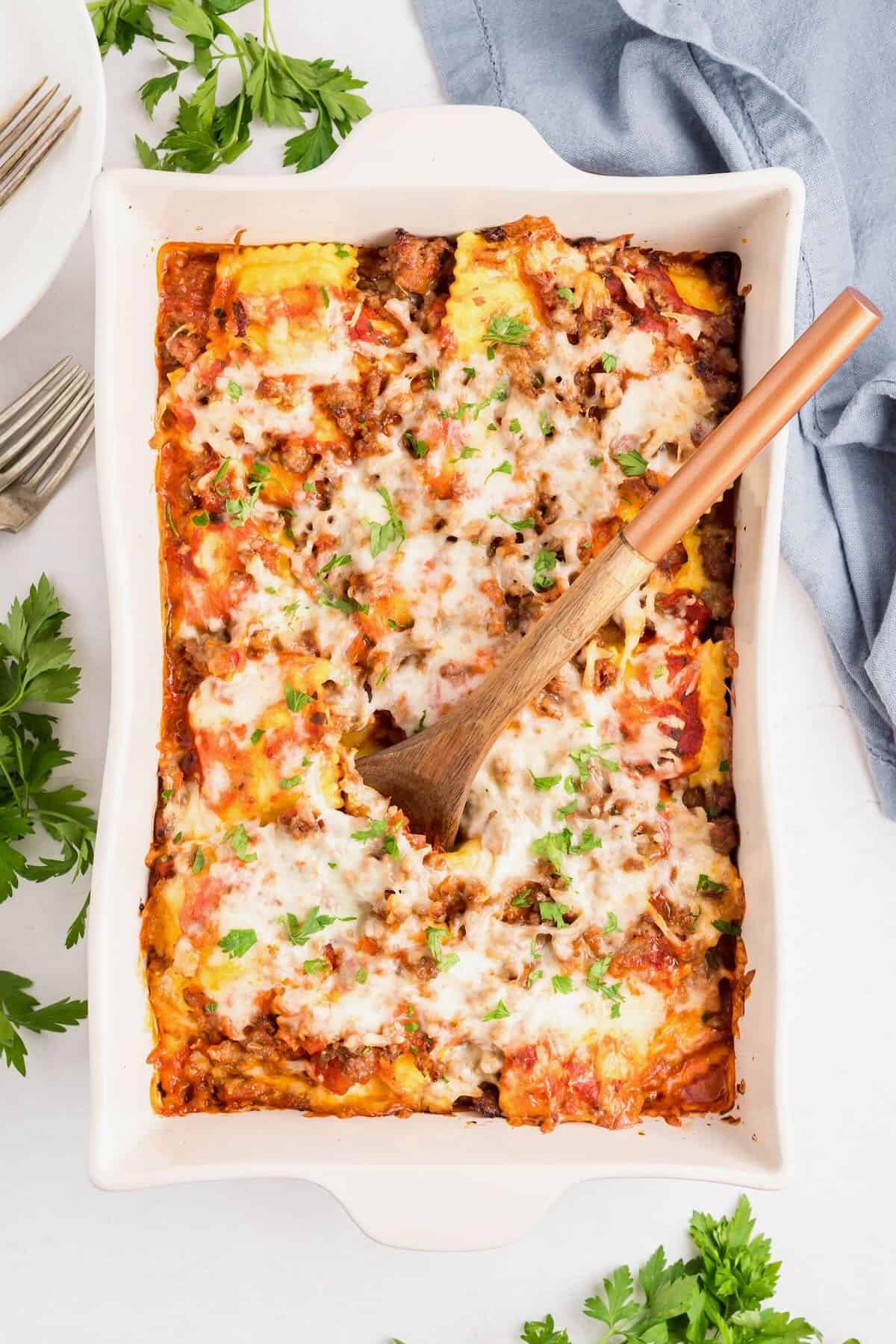 Baked ravioli in a white baking dish with layers of marinara sauce, ravioli, sausage, and melted cheese.