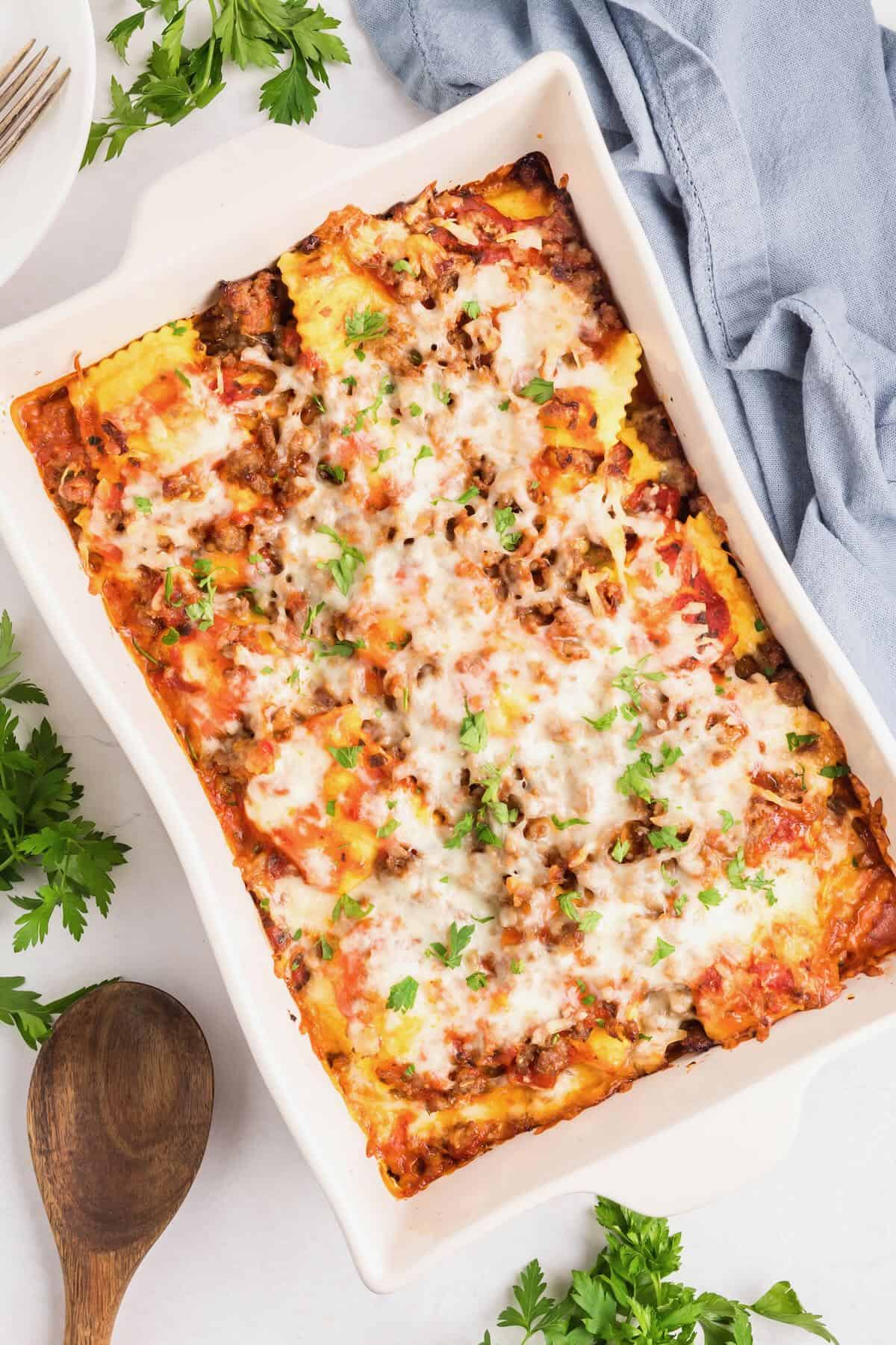 Baked ravioli in a white baking dish with layers of marinara sauce, ravioli, sausage, and melted cheese.
