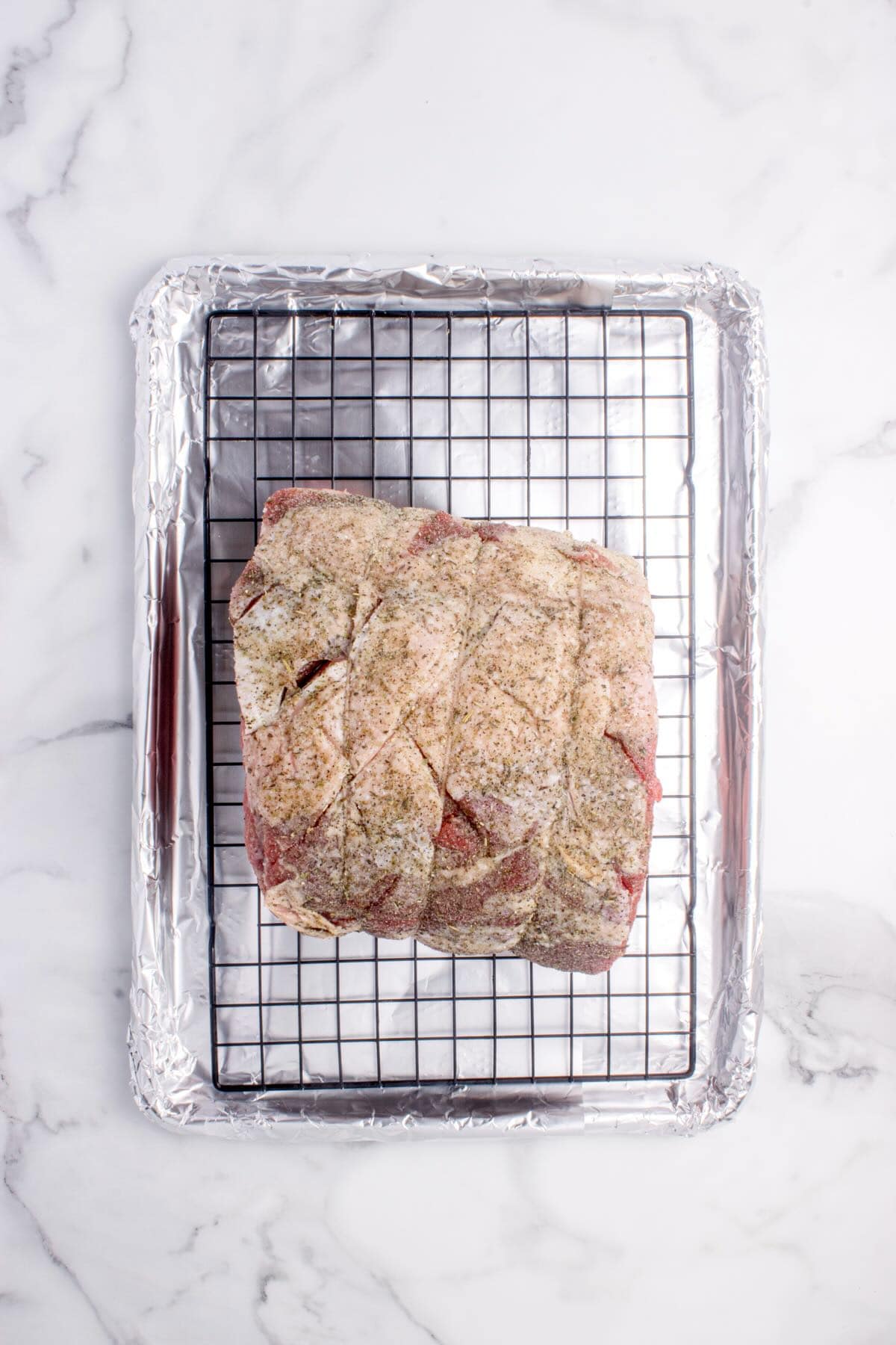 A raw boneless prime rib roast tied with twine and seasoned on a rack in a rimmed baking sheet.