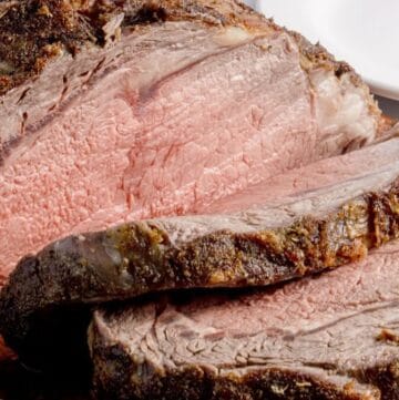 A boneless prime rib roast sliced on a cutting board garnished with sprigs of rosemary.