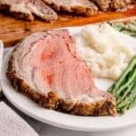 A slice of boneless prime rib roast on a plate with mashed potatoes and asparagus.