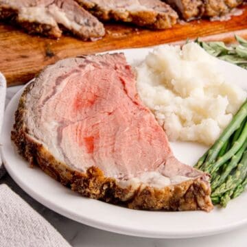 A slice of boneless prime rib roast on a plate with mashed potatoes and asparagus.