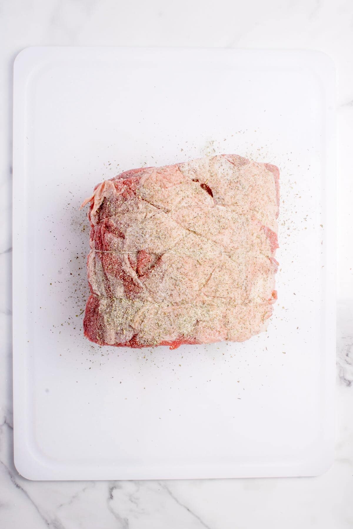 A raw boneless prime rib roast seasoned with salt, pepper, italian seasoning and garlic and onion powder.