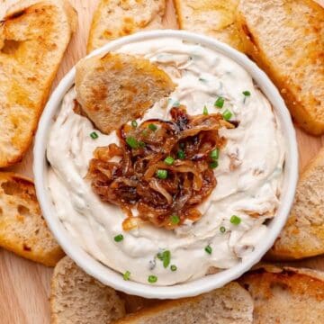 A bowl of caramelized-onion dip, topped with caramelized onions, surrounded by crostini.