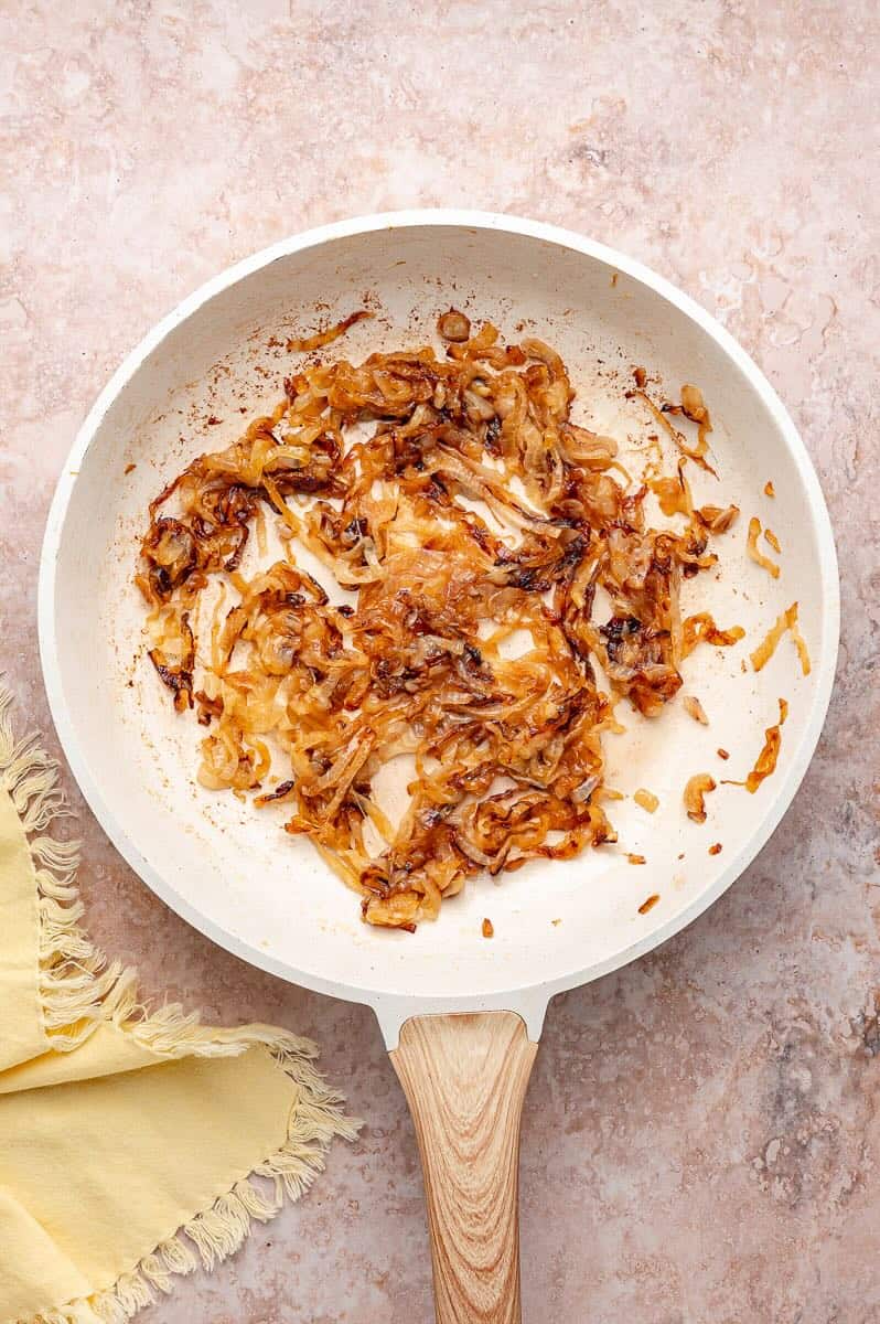 Onion slices are cooking in a skillet until they are caramelized.