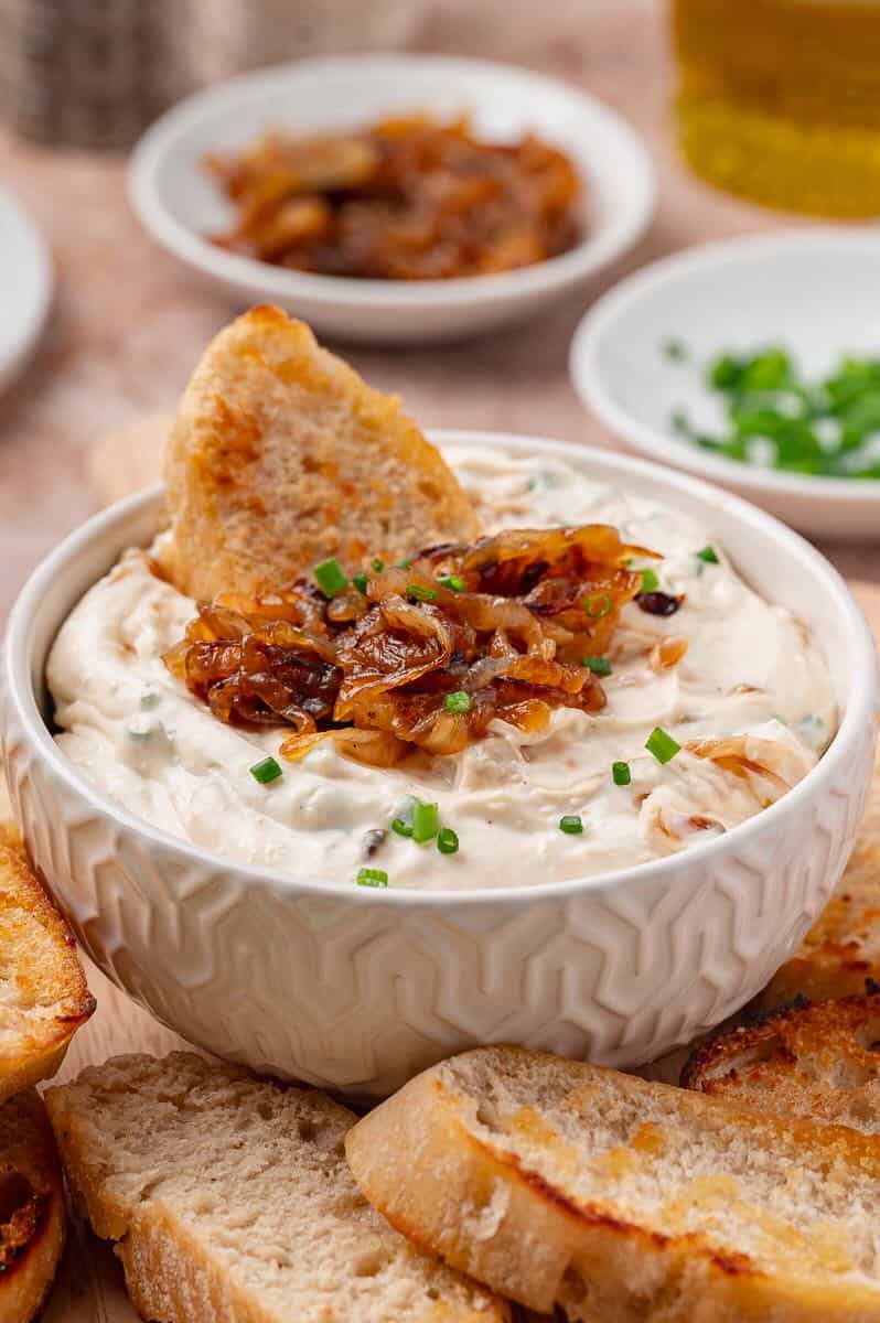 Caramelized onion dip in a bowl with crostini and garnished with more caramelized onions.